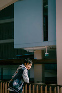 Side view of man standing by railing against building