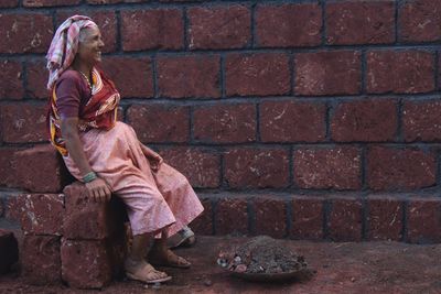 Full length of female worker sitting by brick wall at construction site