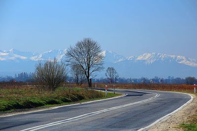 Empty road along trees and landscape against blue sky