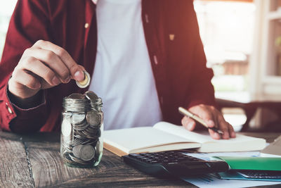 Midsection of businessman putting coins in jar 