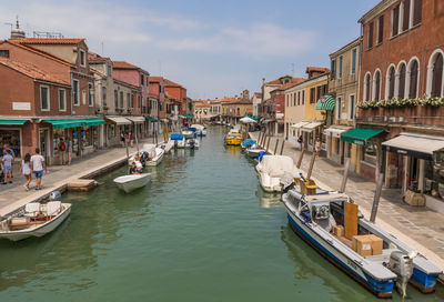 Boats in canal amidst buildings in city against sky