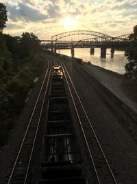 Railway bridge over river against sky during sunset