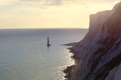 High angle view of lighthouse in sea by cliff against sky