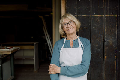 Portrait of smiling senior entrepreneur standing at hardware store entrance