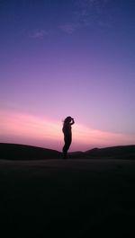 Silhouette woman standing on desert against clear sky during sunset