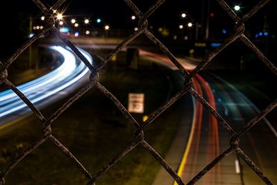Close-up of light trails on chainlink fence at night