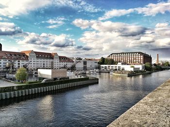 Buildings by river against sky in city