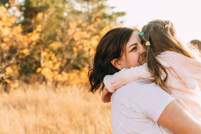 Beautiful young woman and her charming little daughter are hugging and smiling outdoors