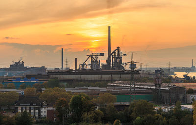Factory by buildings against sky during sunset