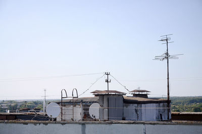 Electricity pylon by buildings against clear sky