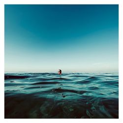 Man swimming in sea against clear blue sky