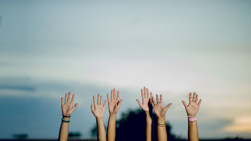 Cropped hands raised against sky during sunset