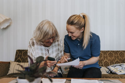 Happy female caregiver explaining medical reports to senior woman sitting at home