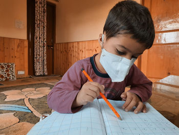 Boy wearing mask writing in book