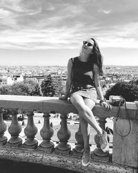 Full length of woman sitting on retaining wall against sky