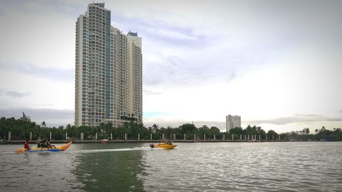 Scenic view of river by cityscape against sky