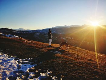 Woman and dog enjoying the view from top of the mountain during sunset 