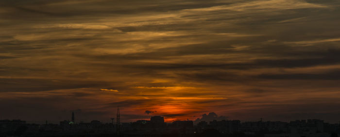 Silhouette of city against cloudy sky during sunset