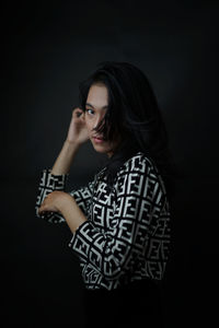 Portrait of woman standing against black background