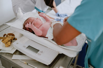 From above side view of crop medical specialist weighting newborn baby on scale in modern hospital