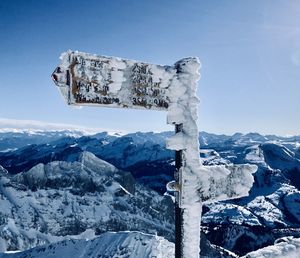 Snow covered information sign on mountain against sky