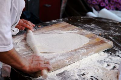 Midsection of chef rolling dough on board