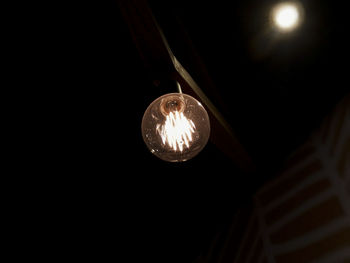 Low angle view of illuminated light bulb hanging against black background