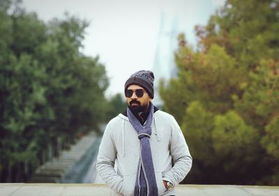 Man wearing sunglasses standing by retaining wall against trees