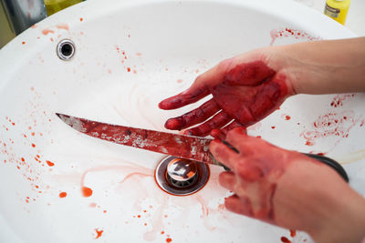 Cropped bloody hands of woman holding knife in sink