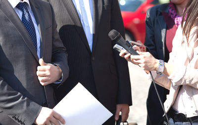 Midsection of journalist holding microphone in front of businessmen