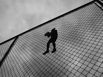 Low angle view of silhouette human shape paper craft attached on chainlink fence