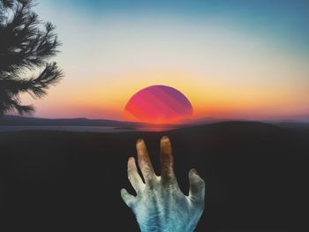 Person hand against orange sky during sunset