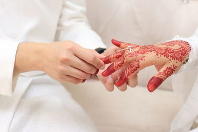 Midsection of groom holding bride finger on sofa during wedding