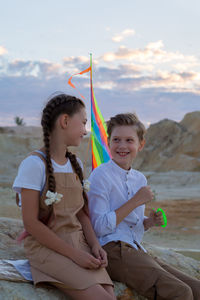 Friends a boy and a girl are sitting on a rock in the mountains before launching a kite.