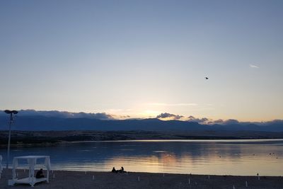 Silhouette birds flying over lake against sky during sunset