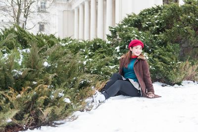 Portrait of young woman sitting on snow covered plants
