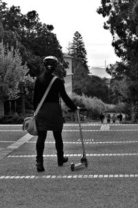 Rear view of woman with push scooter on footpath