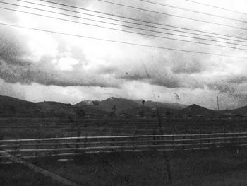 Power lines on landscape against cloudy sky