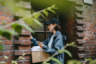 Female delivery person ringing doorbell while arriving with parcel outside house