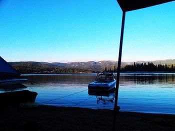 Boats in calm lake against clear blue sky