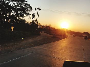 Road amidst silhouette trees against sky during sunset