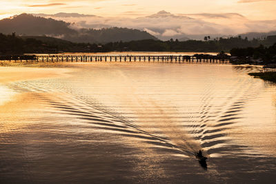 Boat sail on songaria river with mon wooden bridge with mist at sunrise, sangkhlaburi, kanchanaburi