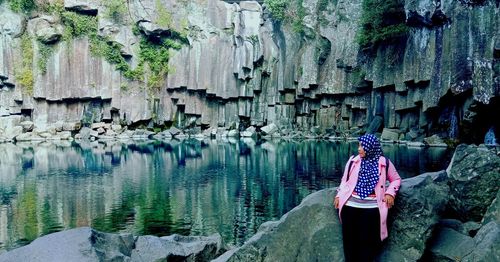 Rear view of woman standing on rock by water