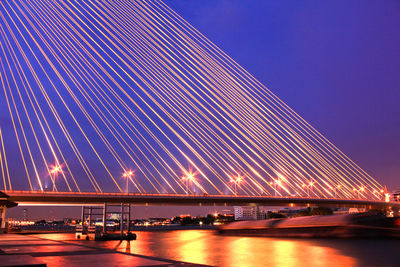 Illuminated bridge against blue sky at night