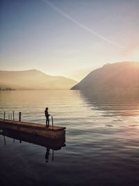 Silhouette fisherman standing on pier by lake against sky