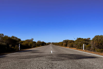 Surface level of empty road against clear blue sky