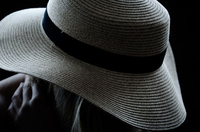 Close-up of person wearing hat against black background