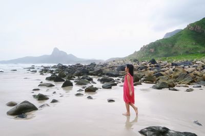 Rear view of woman standing on rock against sky