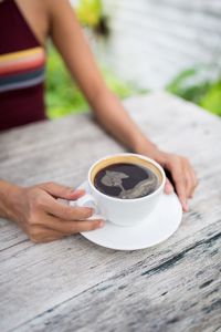 Close-up of woman holding coffee cup on table