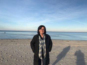 Portrait of smiling mature woman standing at beach during sunset